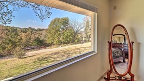 A room with a large window overlooking a grassy area with trees and a house in the distance. A wooden-framed mirror is positioned against the wall. - Large Home w/ Games: 4 Mi to Bull Shoals Lake! (Lakeview)