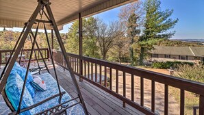 A wooden deck with a swing chair and a view of a house and trees. - Large Home w/ Games: 4 Mi to Bull Shoals Lake! (Lakeview)