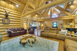 A log cabin interior with a fireplace, leather sofas, a dining area, and a staircase leading to an upper level. - 14 Mi to Slopes: Lodge on 104 Acres in Boyne City (Boyne City)