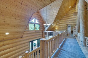 L’intérieur d’un chalet en bois, avec un balcon, un lustre et une vue sur l’extérieur.