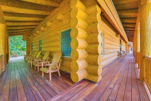 A log cabin with a wooden porch, several Adirondack chairs, and a window with a view of greenery. - 14 Mi to Slopes: Lodge on 104 Acres in Boyne City (Boyne City)