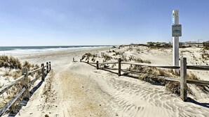 Un sendero arenoso en la playa con cerca de madera y un cartel.