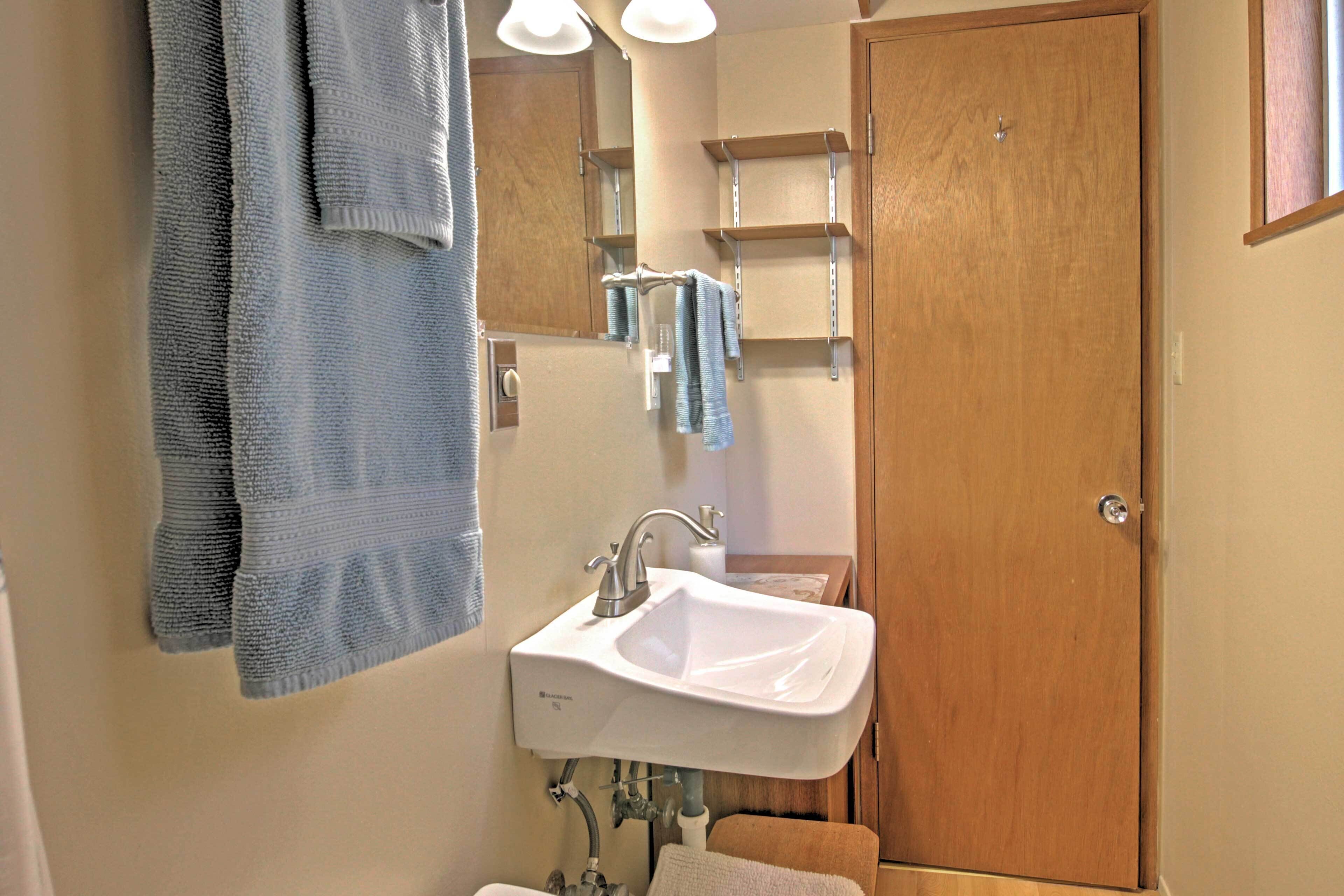 Un baño con lavamanos blanco, puerta de madera y toalleros.