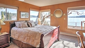 A bedroom with a large bed, a nightstand, a dresser, and a chair. There are two windows with views of a body of water and trees. - Gorgeous Poulsbo Waterfront Home on Liberty Bay! (Poulsbo)