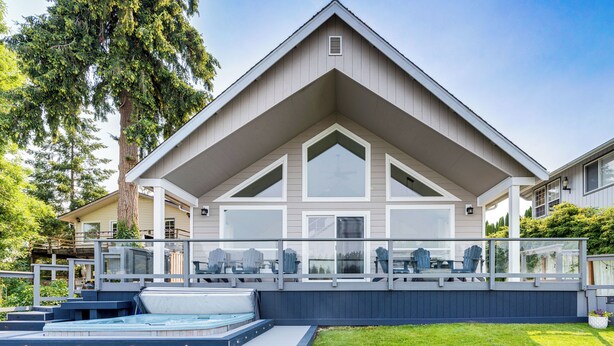 A modern house with a large deck, outdoor hot tub, and a well-maintained lawn.