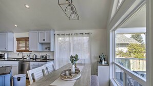 A modern kitchen with white cabinets, a dining table with chairs, a built-in oven, and a large window offering a view of the outdoors.