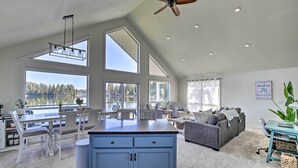 A spacious living area with a kitchen, large windows, and a ceiling fan.