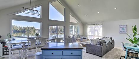 A spacious living area with a kitchen, large windows, and a ceiling fan.