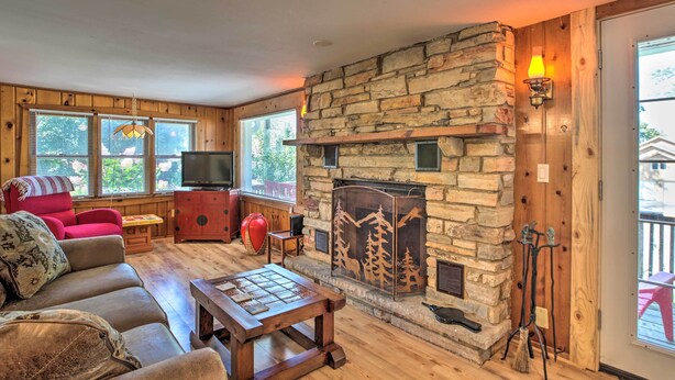 A cozy living room with a stone fireplace, wooden floors, a red sofa, and a television. - Pet-friendly Home w/ Views of Lake Delavan! (Delavan)