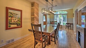 A spacious dining area with a wooden table and chairs, a large painting on the wall, and a view of the outdoors through large windows. - Pet-friendly Home w/ Views of Lake Delavan! (Delavan)