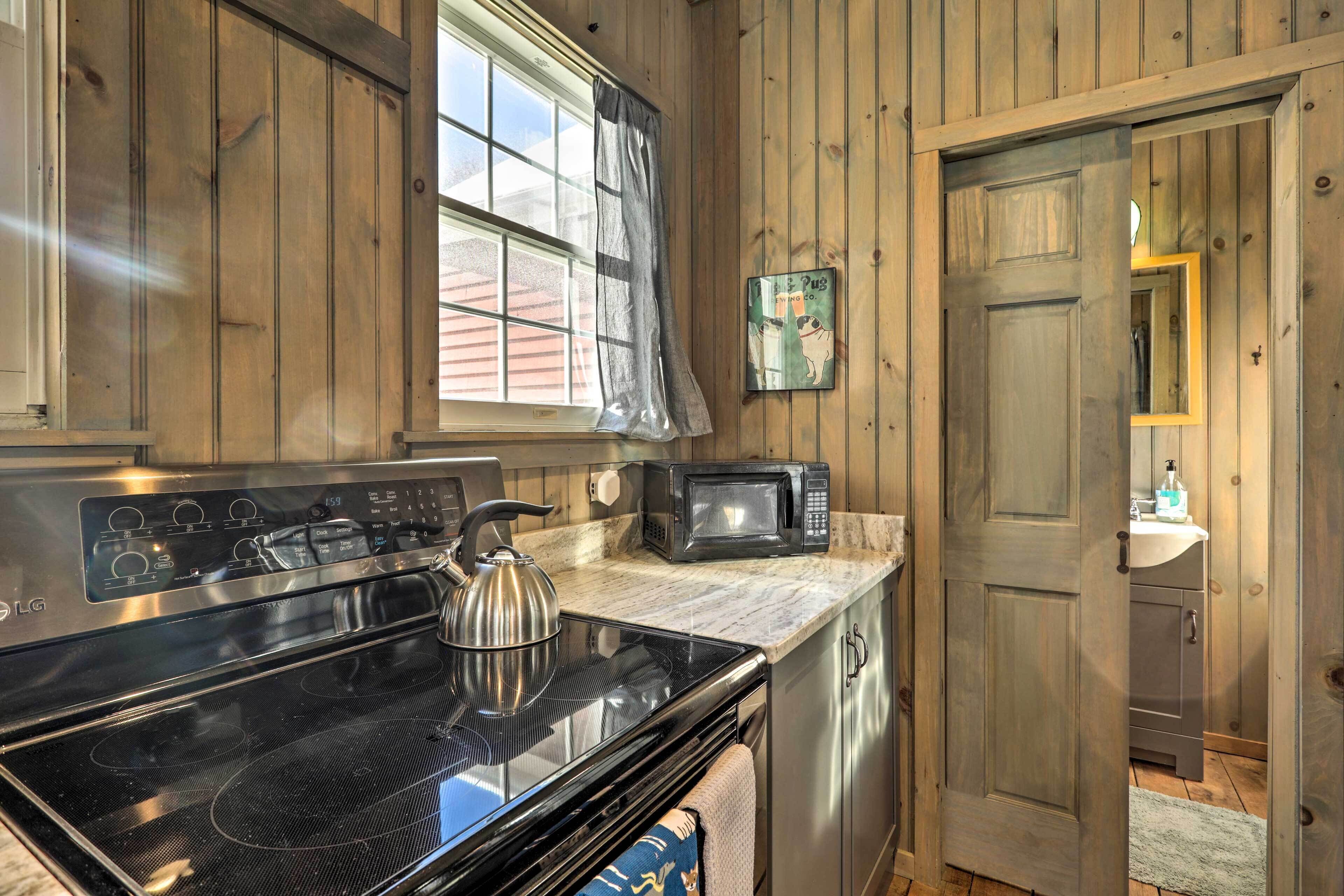 A kitchen with wooden cabinets, a stove, a microwave, and a window with curtains.