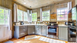 A kitchen with wooden cabinets, a stainless steel refrigerator, and a large window with curtains. - Killingly Barnyard Studio in Wine Country! (Dayville)