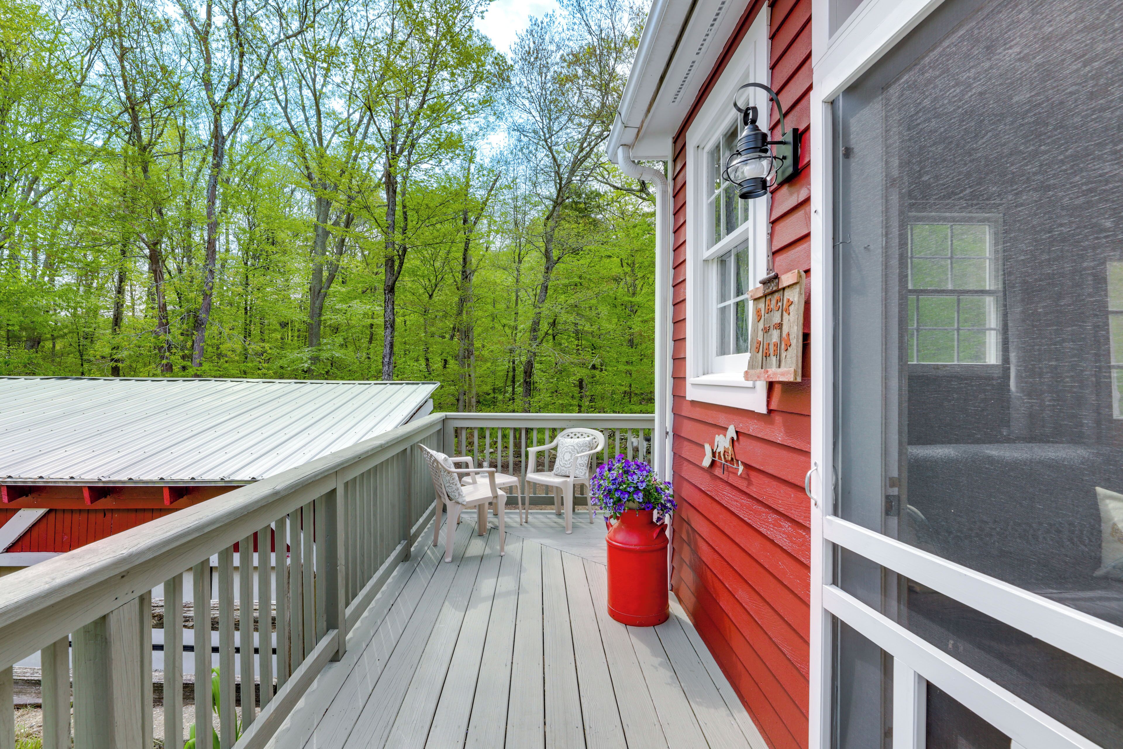 A wooden deck with two white chairs and a red planter with purple flowers.