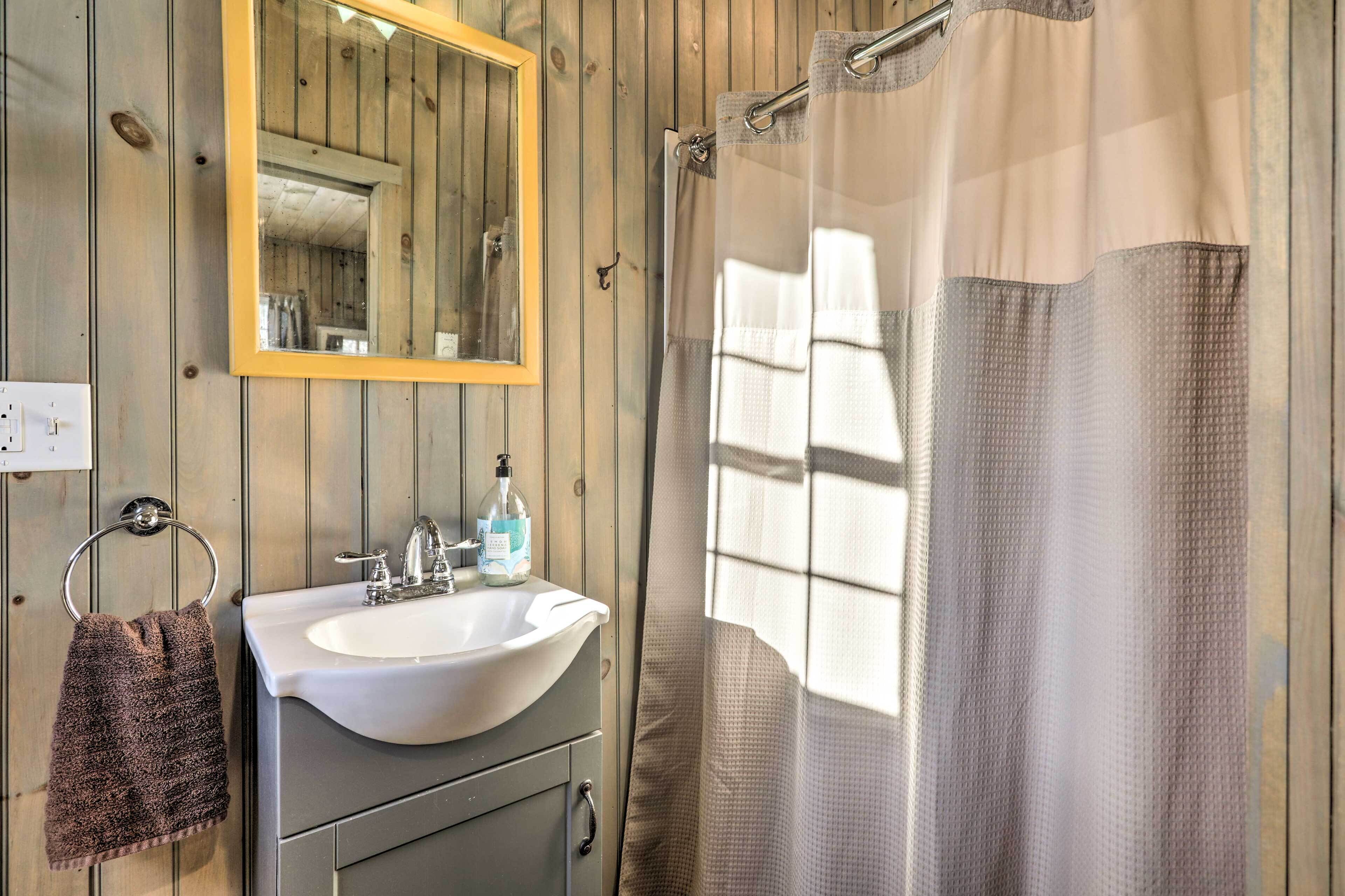 A bathroom with a wooden wall, a white sink, a mirror, and a shower curtain.
