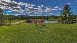 Un campo cubierto de hierba con un lago, una cabaña de madera y una silla roja en primer plano.