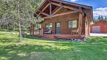 A wooden cabin with a porch, a garage, and a small shed in a wooded area.