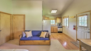 Un espacio habitable compacto con sofá de madera, una mesa de comedor y una zona de cocina con armarios de madera y un refrigerador.