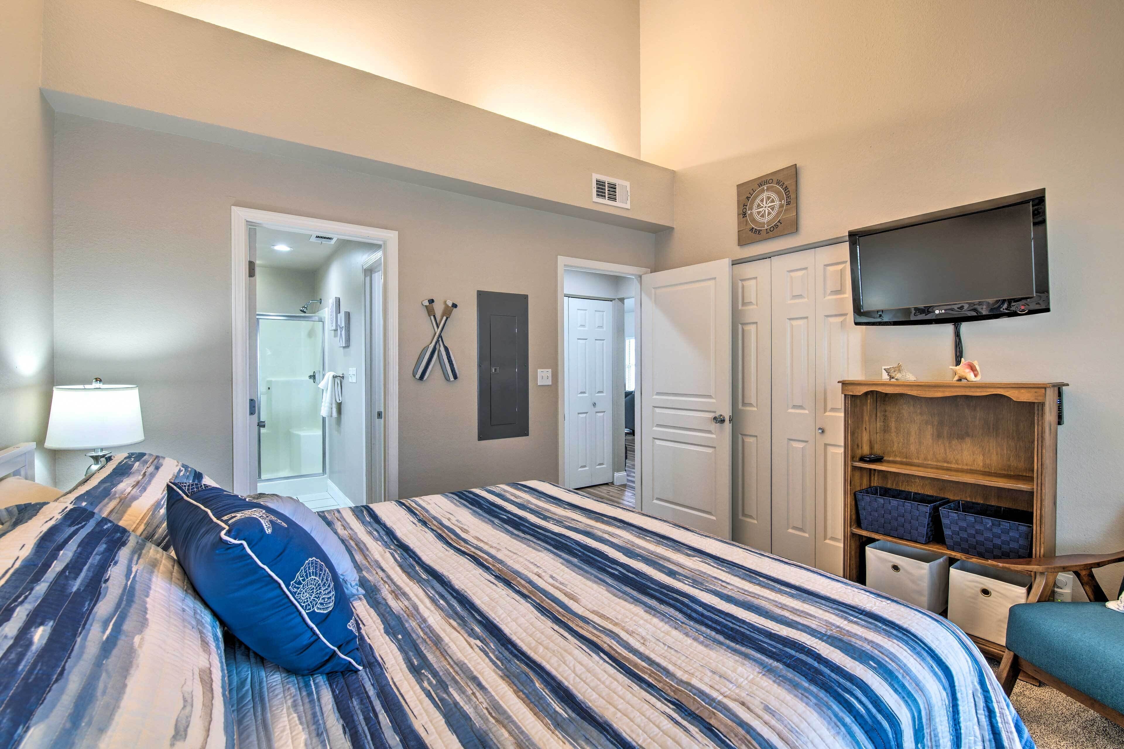 A hotel room with a bed, a TV mounted on the wall, a wooden cabinet with storage bins, and a bathroom visible through an open door.