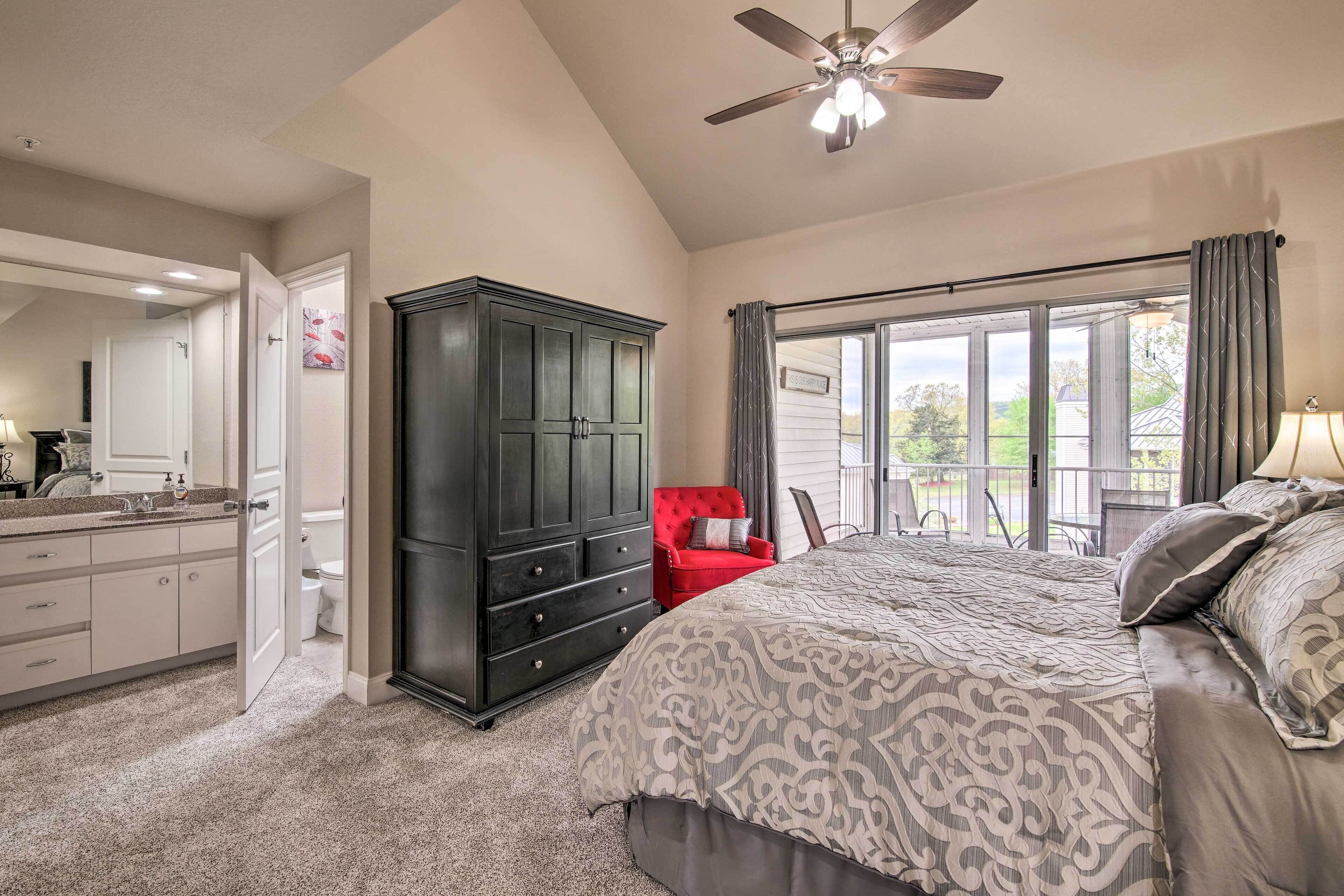 A bedroom with a large bed, a dark wooden dresser, a red chair, and a balcony with a view.