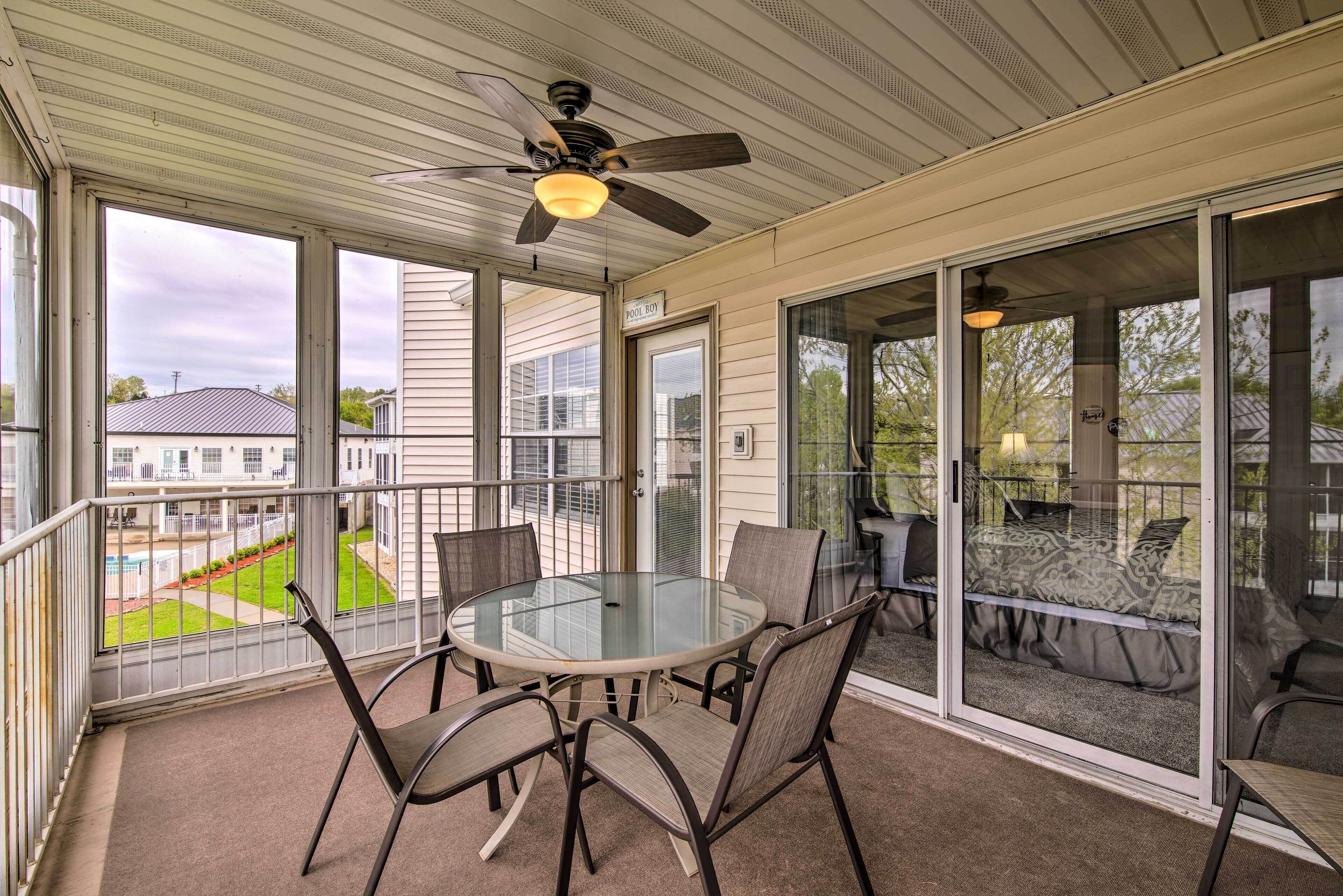 A covered balcony with a glass table and chairs, a ceiling fan, and a view of neighboring houses.