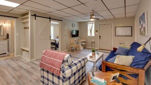 Un salon avec un canapé à carreaux, une table basse et un téléviseur. Une porte coulissante donne accès à une autre pièce.