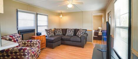 A living room with a sectional sofa, a patterned armchair, a small table, and a ceiling fan.