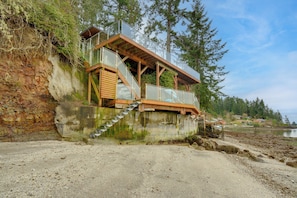 En kystnær trækonstruktion med gelænder i glas, trapper og udsigt til strand og vand.
