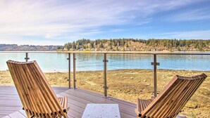 Una terraza de madera con dos sillas Adirondack mirando un lago, una barandilla metálica y vistas a un promontorio cubierto de bosque.