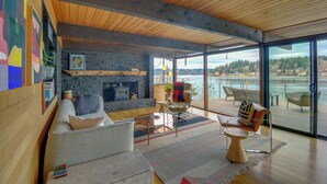Un salón moderno con chimenea, asientos cómodos y un amplio ventanal que da a un balcón con vistas al agua.