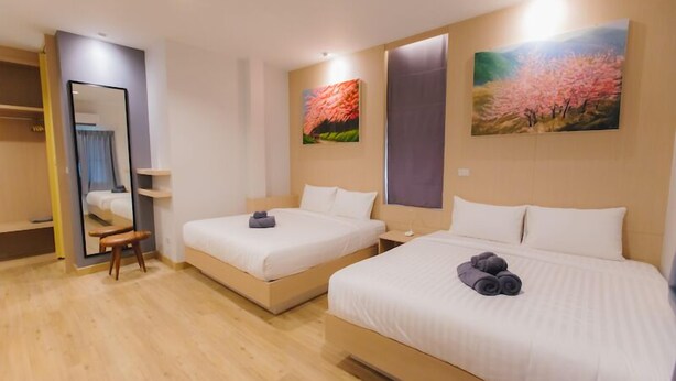 Habitación de hotel con dos camas, un espejo, un banco de madera y obras de arte en las paredes.
