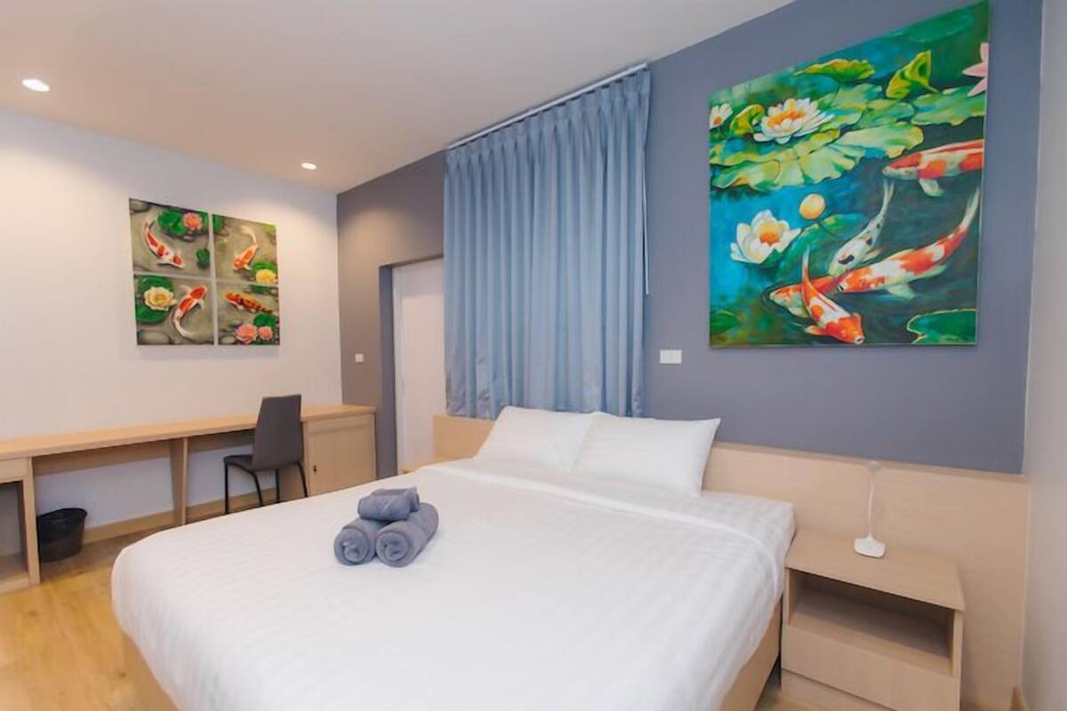 A hotel room with a bed, a desk, and two paintings on the wall.