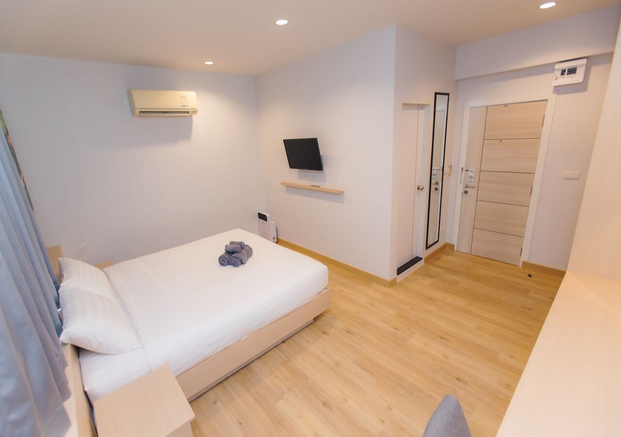 A bedroom with a bed, a TV mounted on the wall, a door, and an air conditioning unit.
