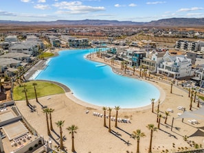 Relax by the resort's large, curved pool surrounded by a sandy beach area and palm trees.