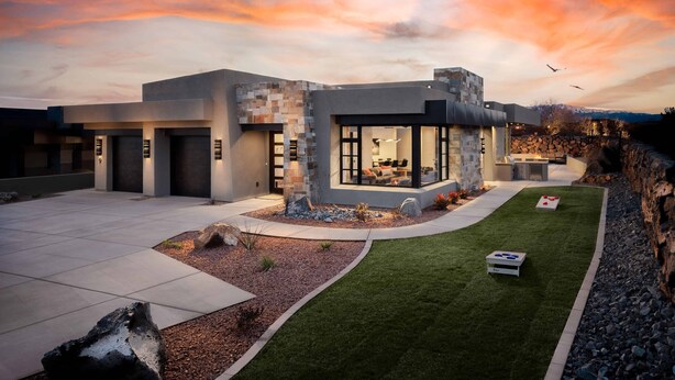 A modern house with a spacious patio, a stone wall, and a well-maintained lawn.