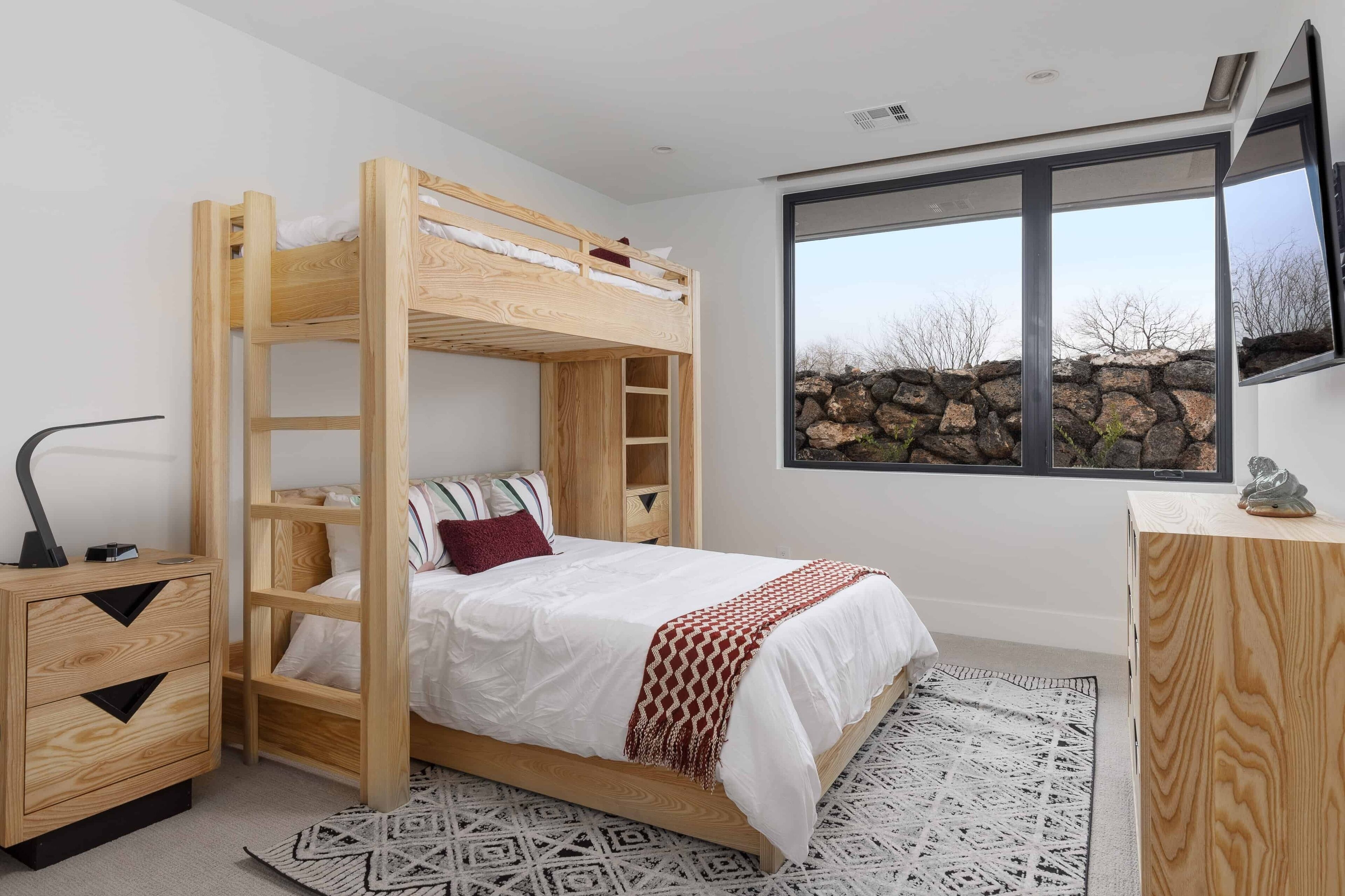 A bunk bed room with a wooden desk and a large window.
