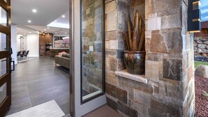 A modern interior with stone walls, a glass door, and a dining area visible through the door.