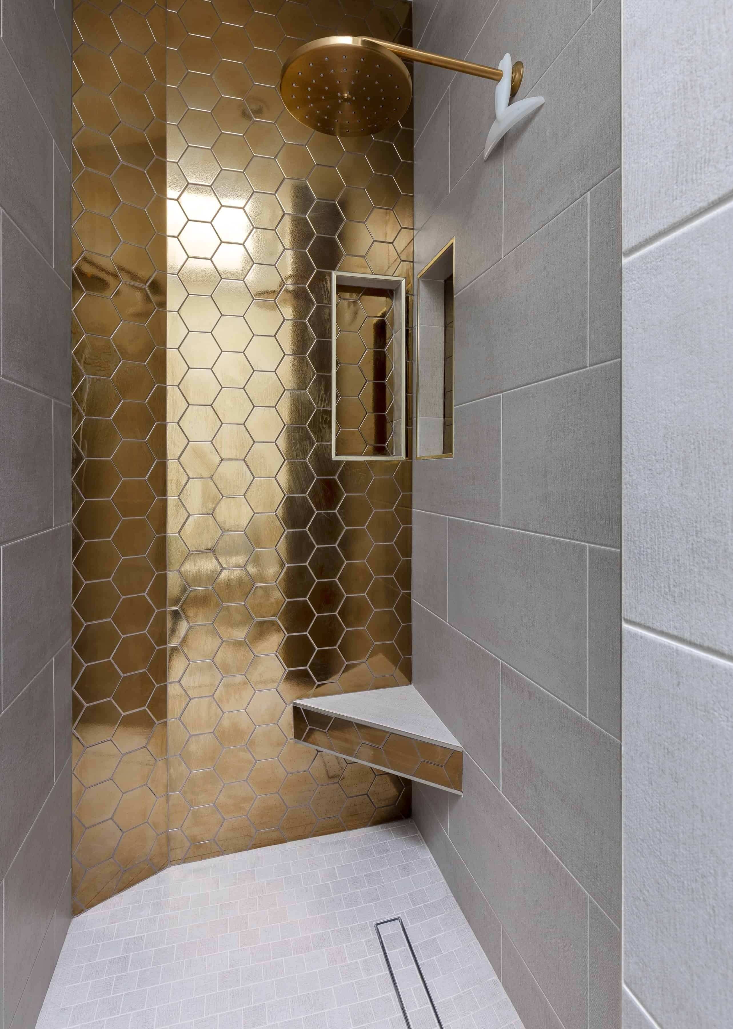 A modern shower area with a hexagonal tile pattern, a gold showerhead, and a built-in shelf.