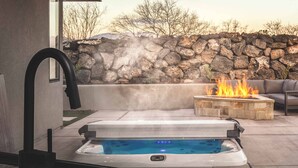 A hot tub with a stone wall and fire feature in the background.