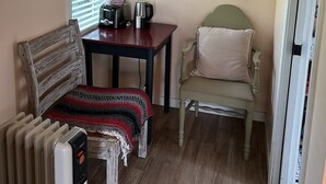 Une pièce chaleureuse avec un banc en bois, une table avec une bouilloire et des tasses, un radiateur, une affiche encadrée et une fenêtre avec des stores.