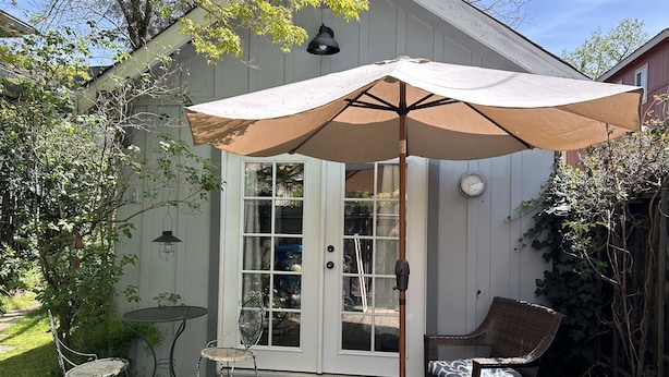 Une terrasse avec une porte blanche, une table, une chaise et un grand parasol.