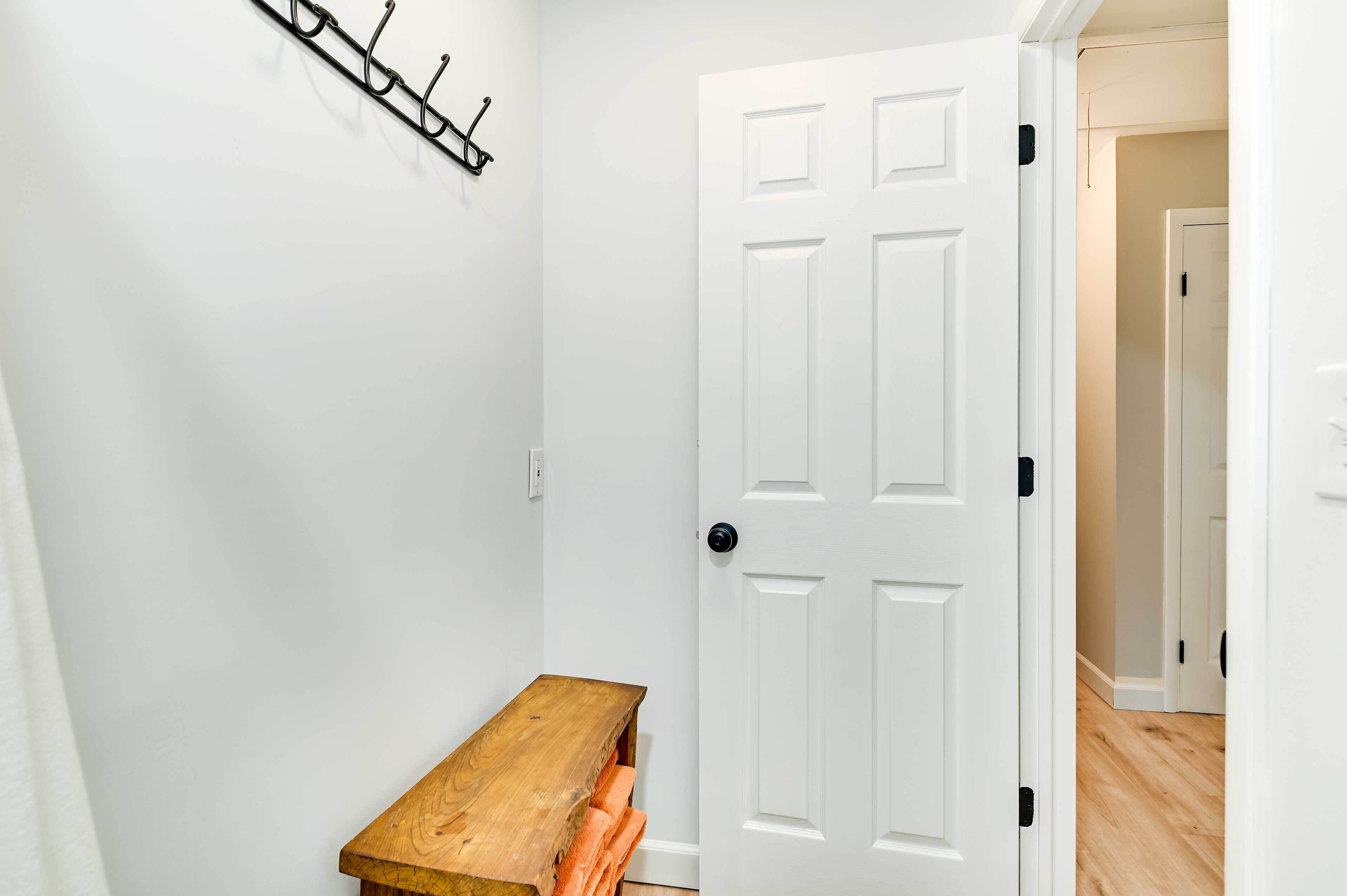 A hallway with a white door, a wooden bench, and a coat rack.