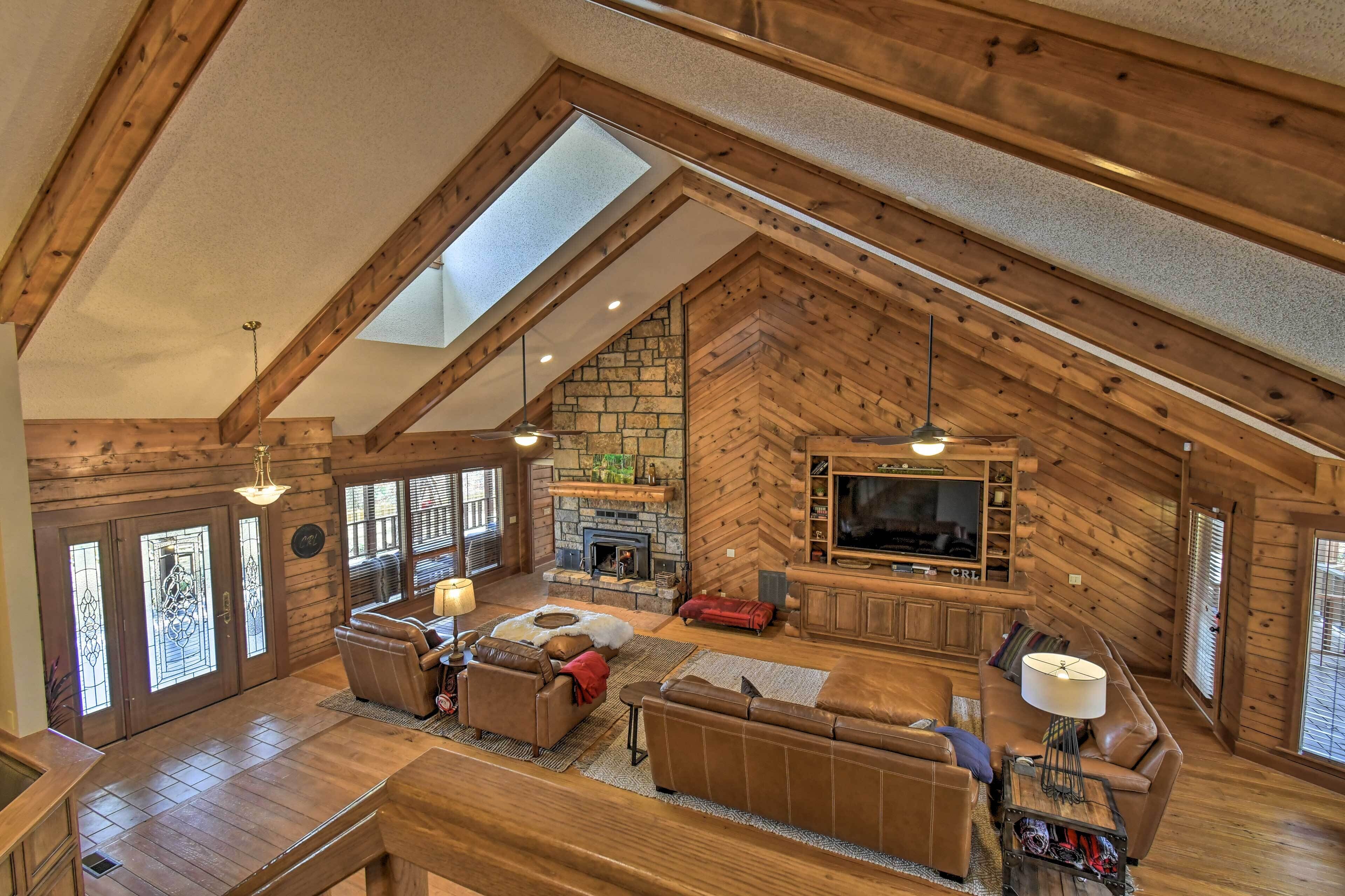 A spacious loft-style living area with a stone fireplace, wooden beams, and a large TV.
