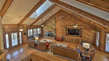 A spacious loft-style living area with a stone fireplace, wooden beams, and a large TV.