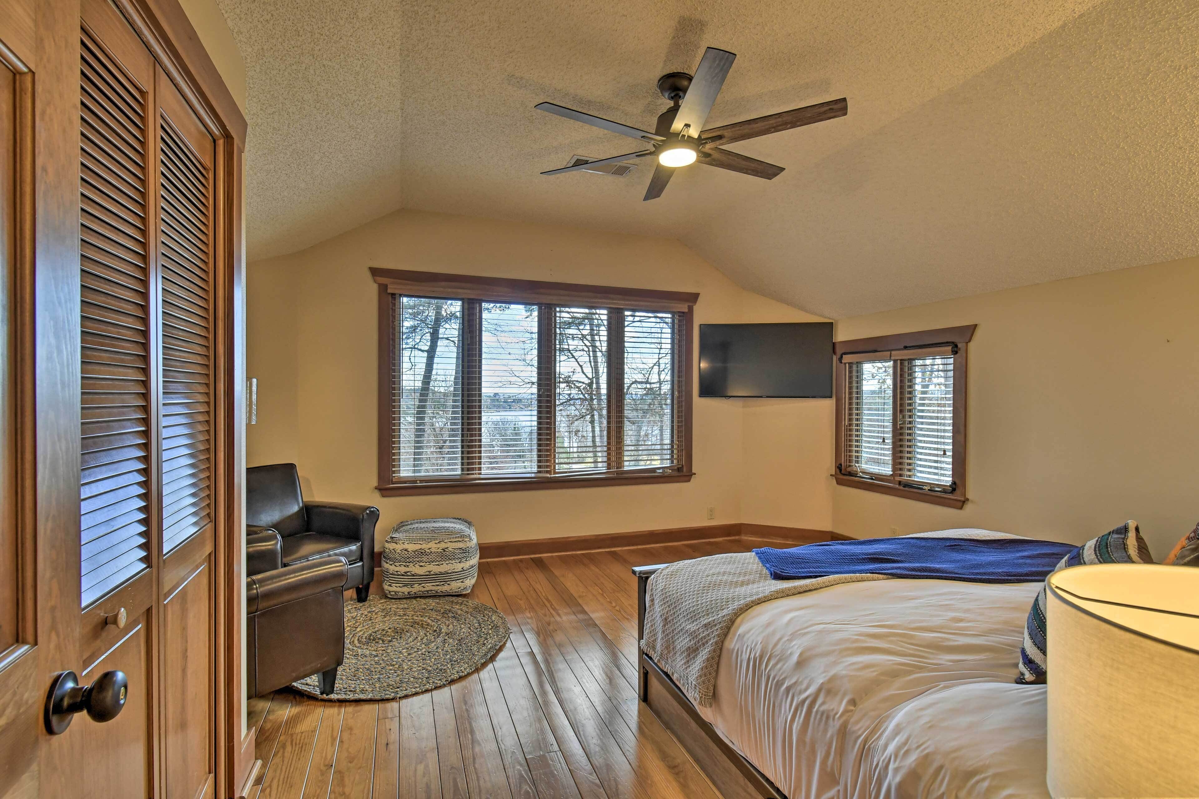 A bedroom with a bed, a ceiling fan, a window, a chair, and a television.