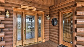 A wooden log cabin entrance with a welcome sign, a glass door, and a window with blinds.