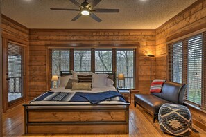 A wooden cabin bedroom with a large bed, a bench, and a ceiling fan. - Hot Tub, Grill: Hilltop Log Cabin in Hot Springs! (Hot Springs)