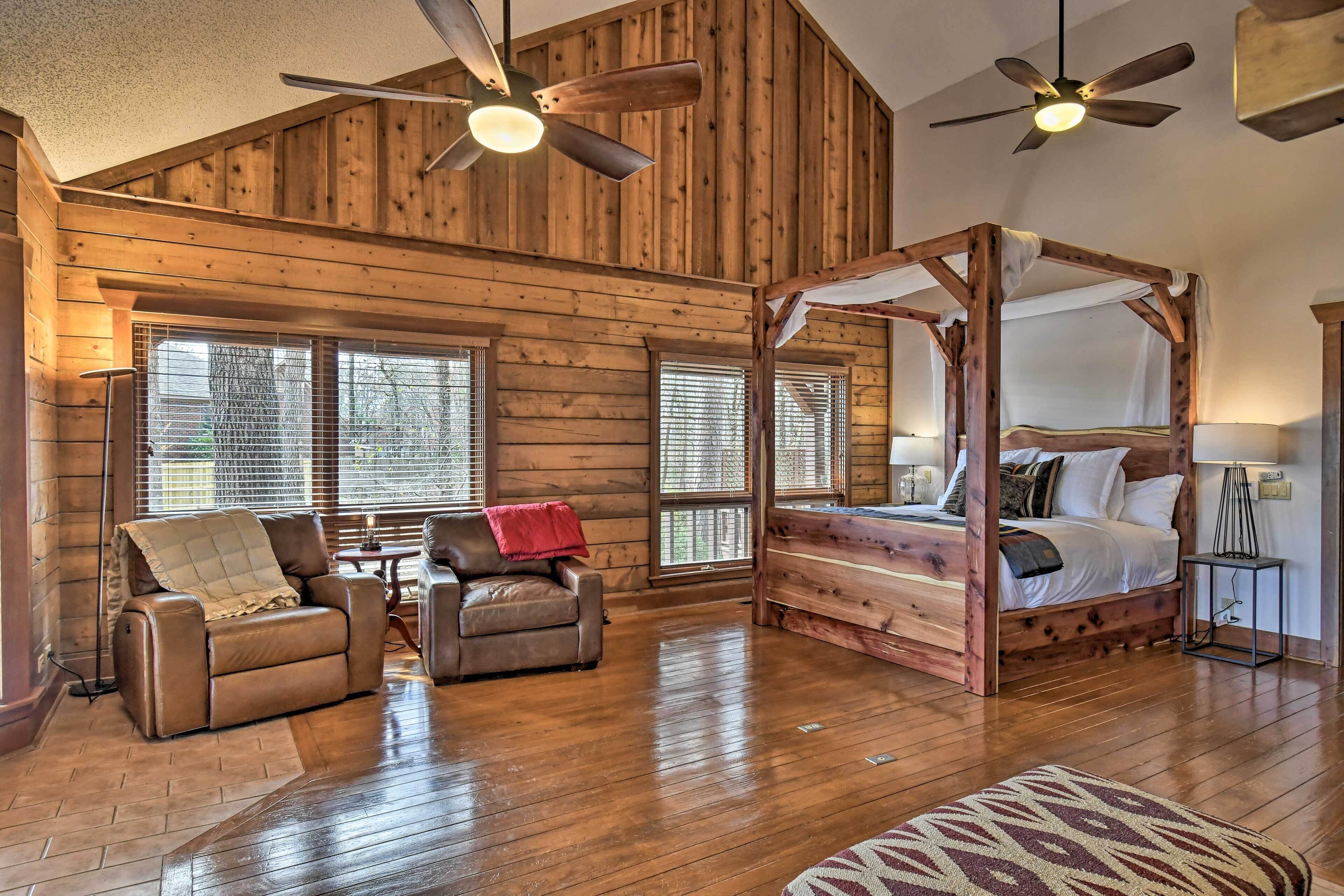 A log cabin interior with a four-poster bed, leather recliner, and a ceiling fan.