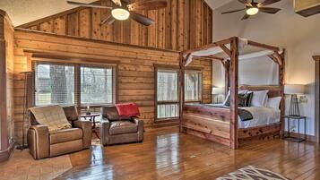 A log cabin interior with a four-poster bed, leather recliner, and a ceiling fan.