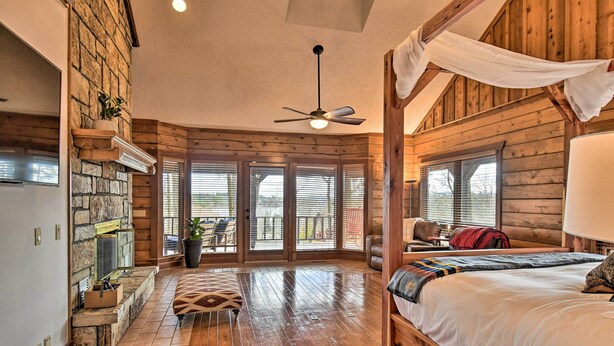 A log cabin-style bedroom with a wooden bed, a ceiling fan, and a stone fireplace. - Hot Tub, Grill: Hilltop Log Cabin in Hot Springs! (Hot Springs)