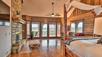 A log cabin-style bedroom with a wooden bed, a ceiling fan, and a stone fireplace.